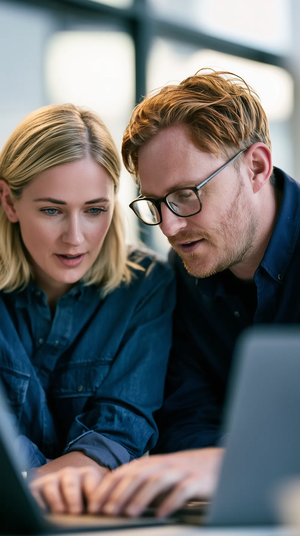 Two professionals reviewing documents on a laptop in an office