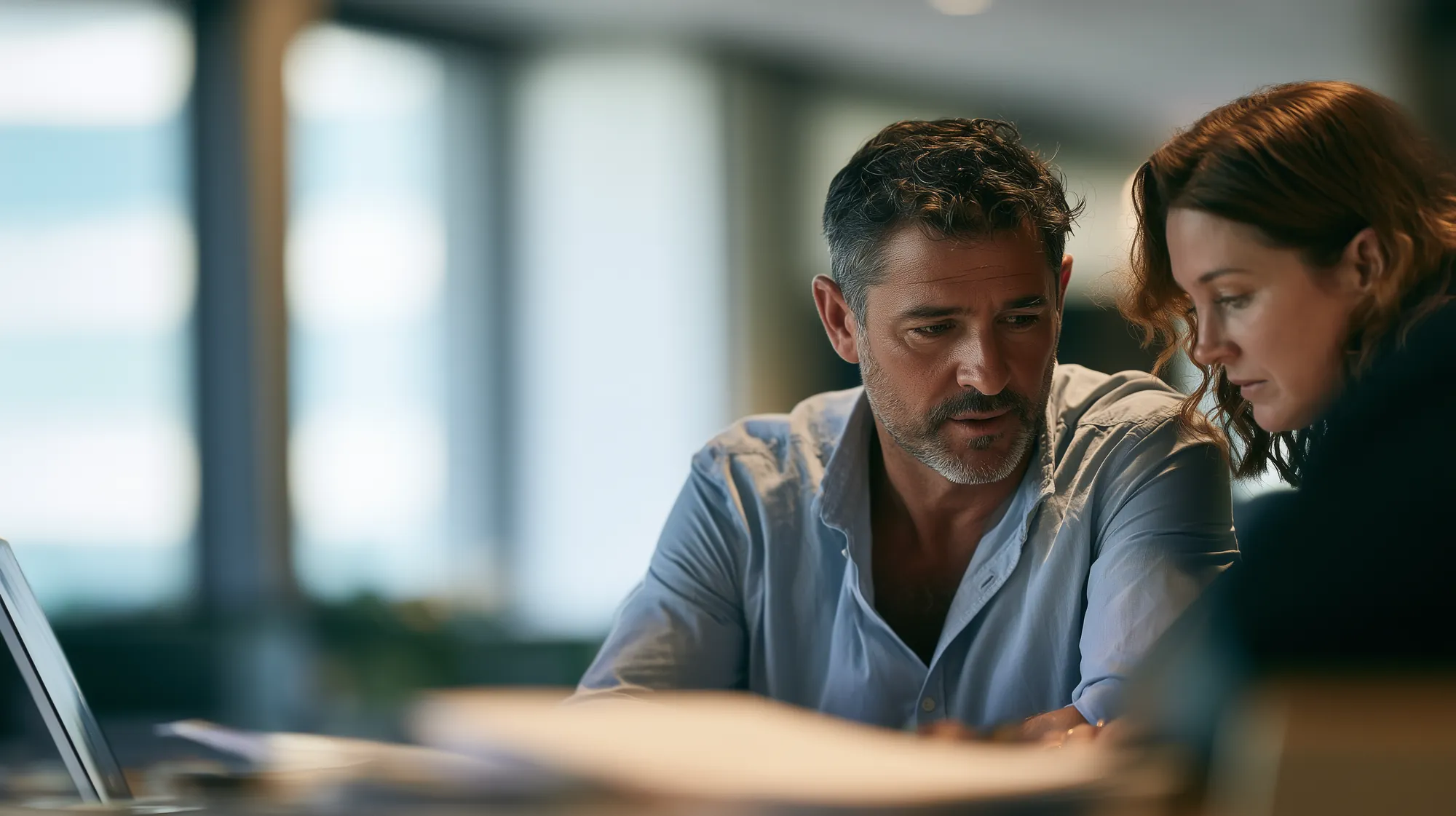 Two accountants reviewing paperwork beside a laptop
