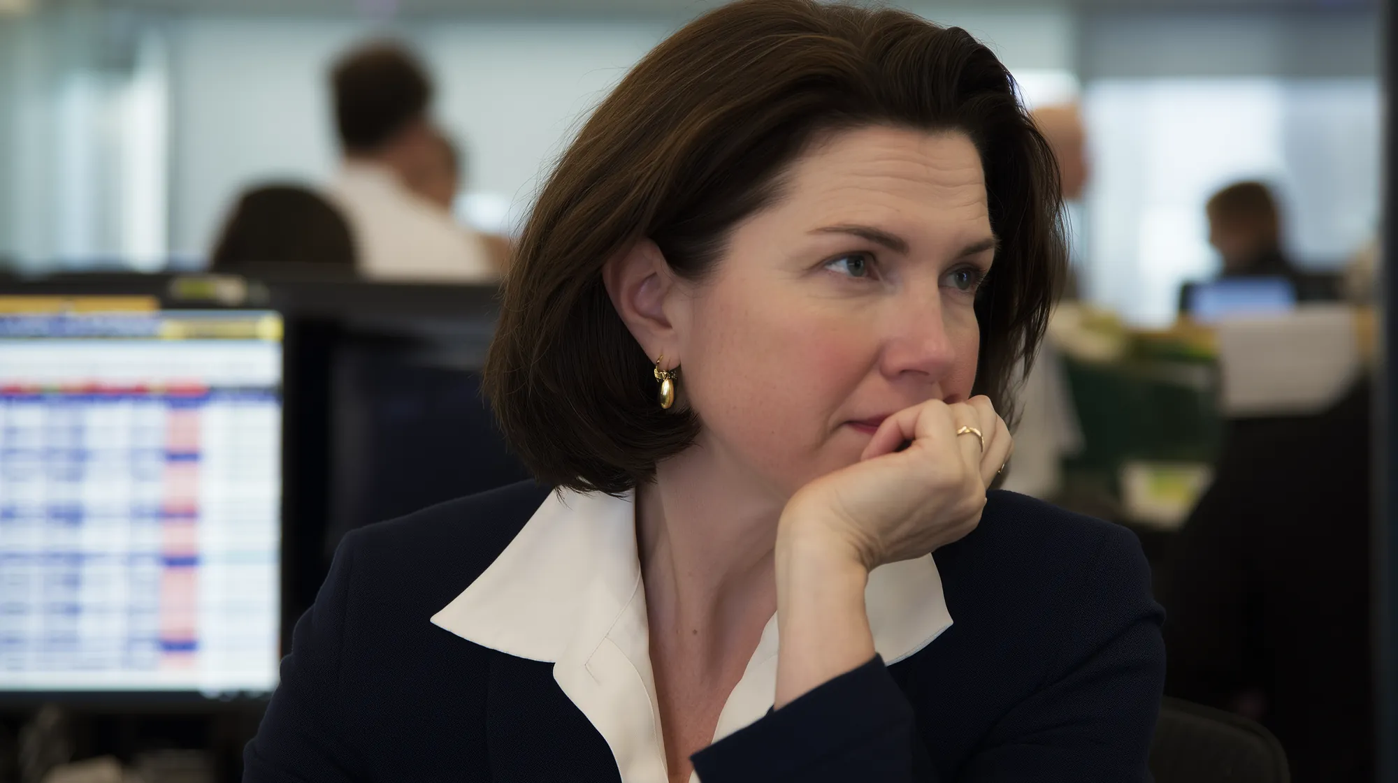 A general manager, chin on her hand, frowning at the spreadsheets on her screen