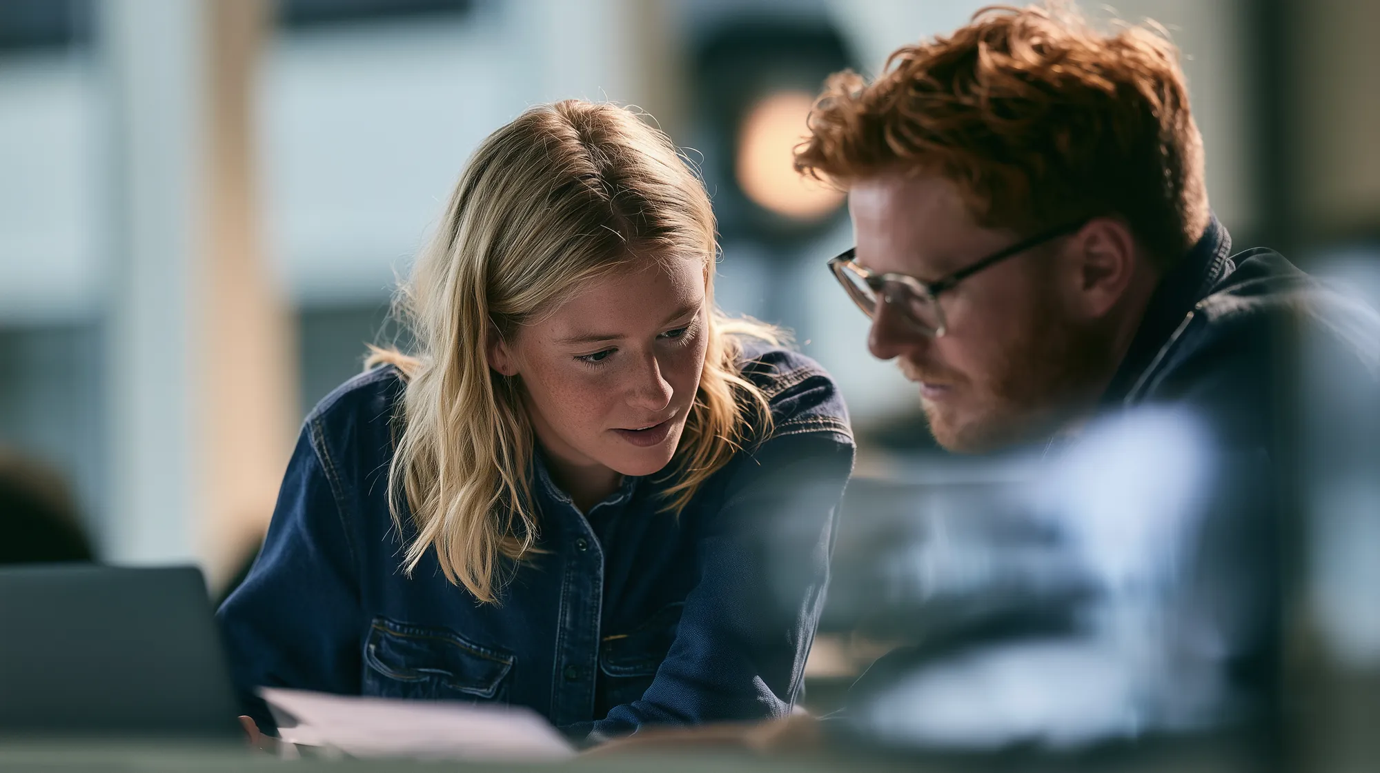 Two professionals reviewing documents on a laptop in an office